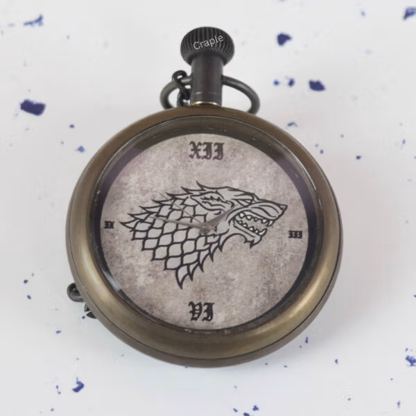 A close-up of the pocket watch dial, showing the detailed Direwolf sigil and vintage-style Roman numerals.