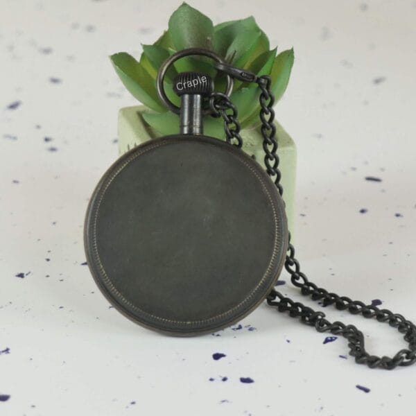 The back view of the antique brass pocket watch, showing its smooth, plain surface and the attached chain.