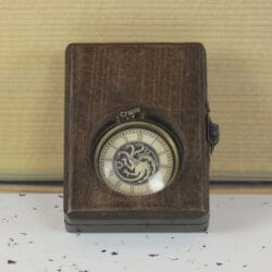 The antique brass pocket watch with a dragon dial visible through the glass window of its closed wooden display box.