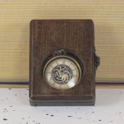The antique brass pocket watch with a dragon dial visible through the glass window of its closed wooden display box.