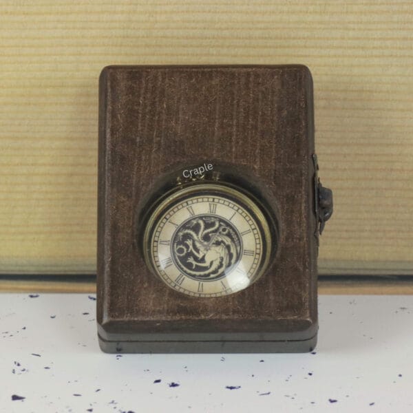 The antique brass pocket watch with a dragon dial visible through the glass window of its closed wooden display box.