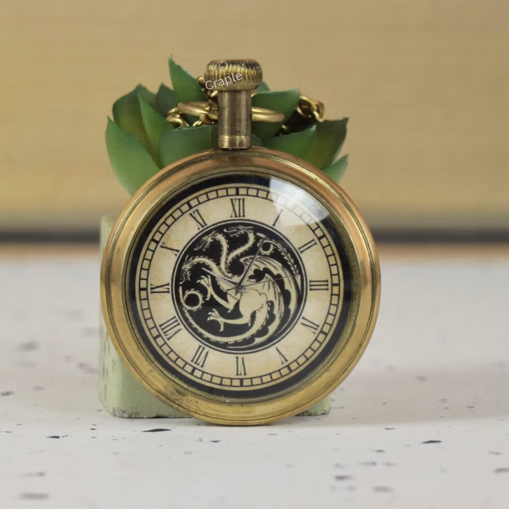 Close-up of an antique brass pocket watch featuring a three-headed dragon motif on the dial with Roman numerals.
