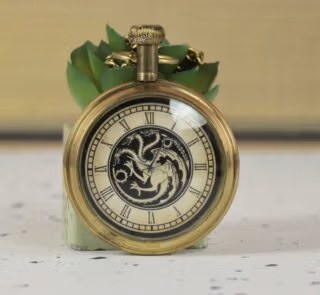 Close-up of an antique brass pocket watch featuring a three-headed dragon motif on the dial with Roman numerals.