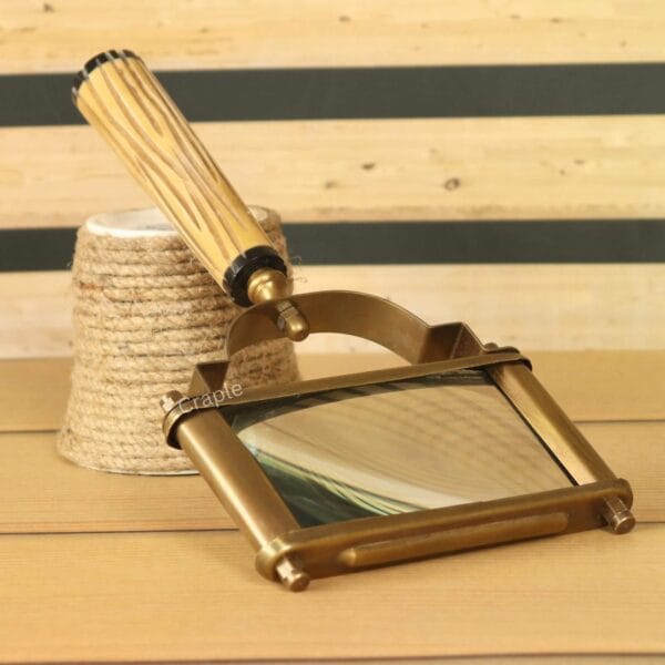 Angled view of a rectangular reading magnifier with an antique brass frame and a fluted wooden handle on a desktop.