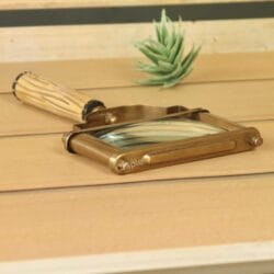 Vintage rectangular magnifying glass with a fluted handle propped against a decorative object on a wooden surface.