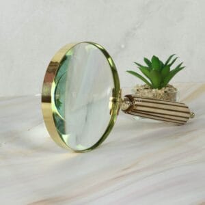 Close-up of a vintage-style magnifying glass with a polished brass rim and a detailed, fluted striped handle.