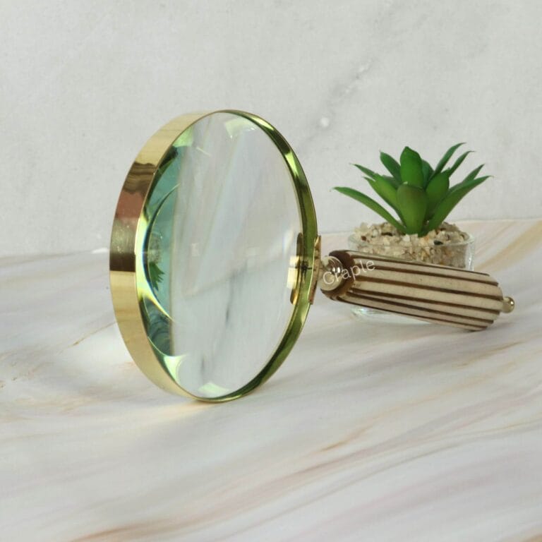 Close-up of a vintage-style magnifying glass with a polished brass rim and a detailed, fluted striped handle.