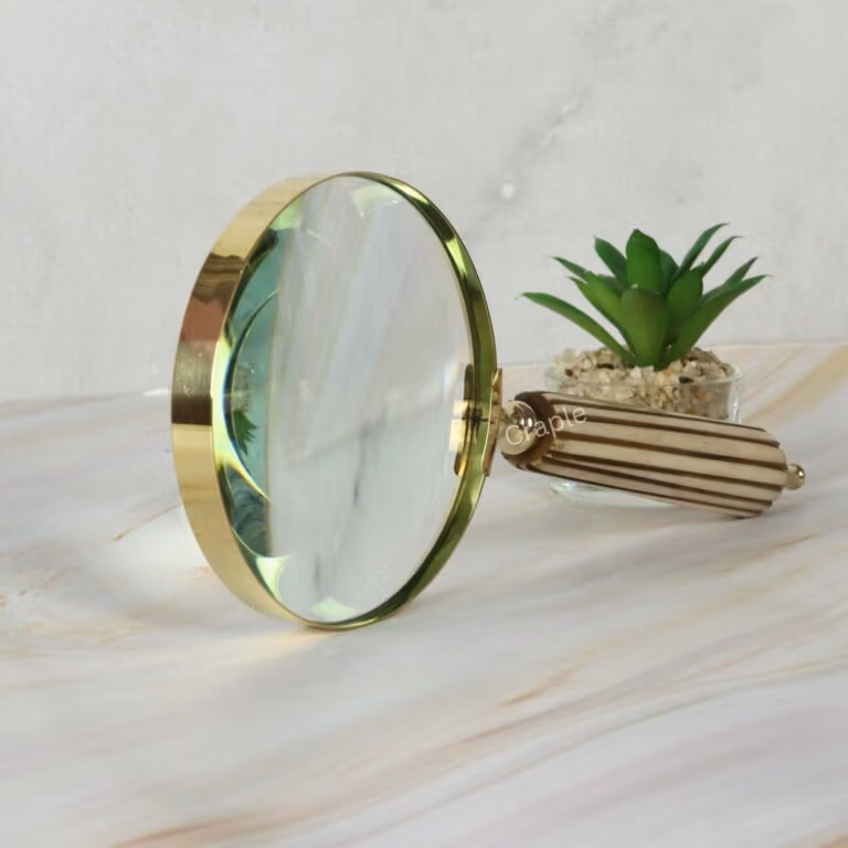 Close-up of a vintage-style magnifying glass with a polished brass rim and a detailed, fluted striped handle.