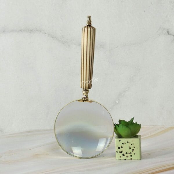 The elegant fluted brass handle of the magnifying glass standing upright on a marble surface.