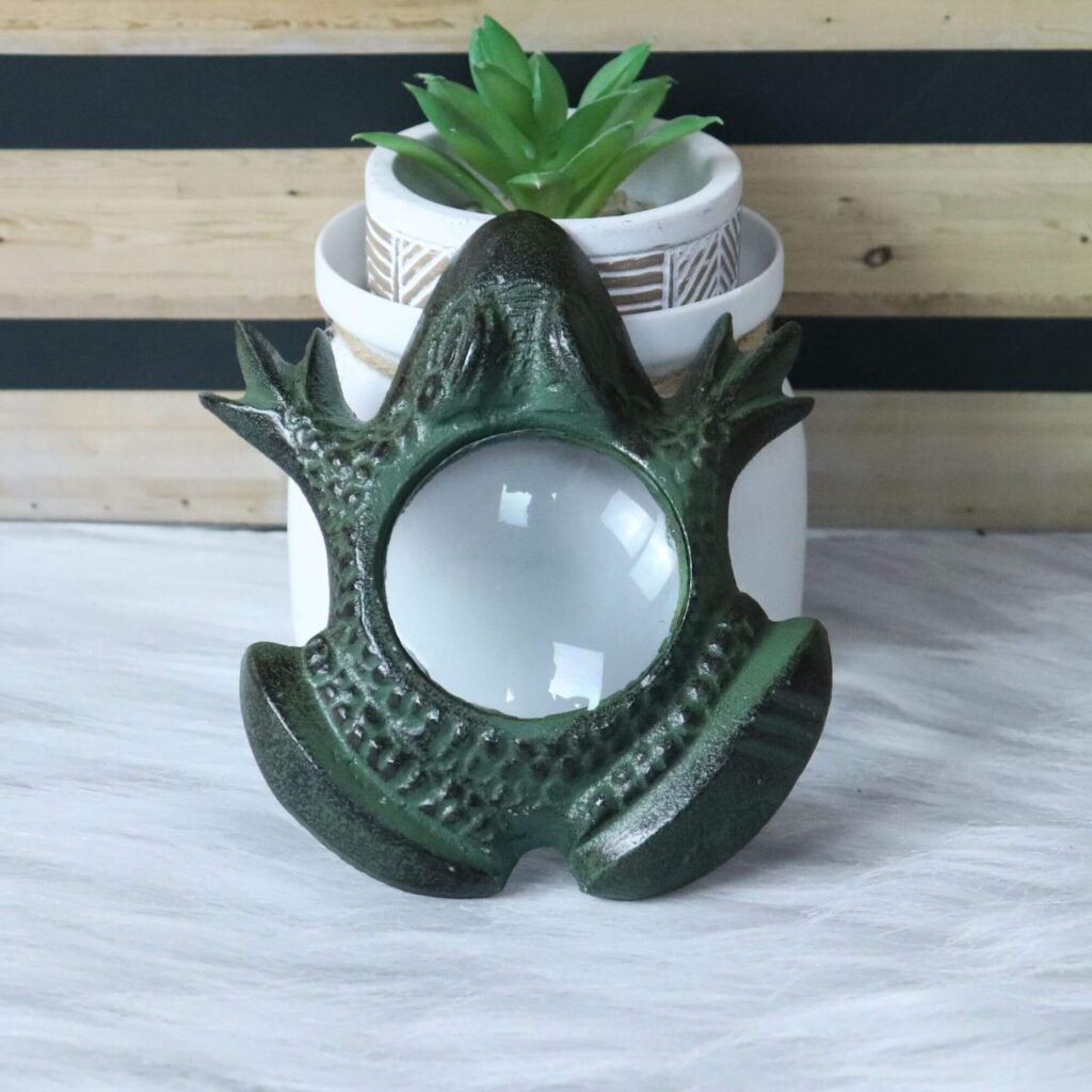 Antique green brass frog magnifying glass standing upright on a desk next to a small plant.