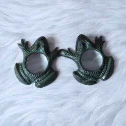 Two frog-shaped paperweight magnifiers positioned face to face on a white fur surface.