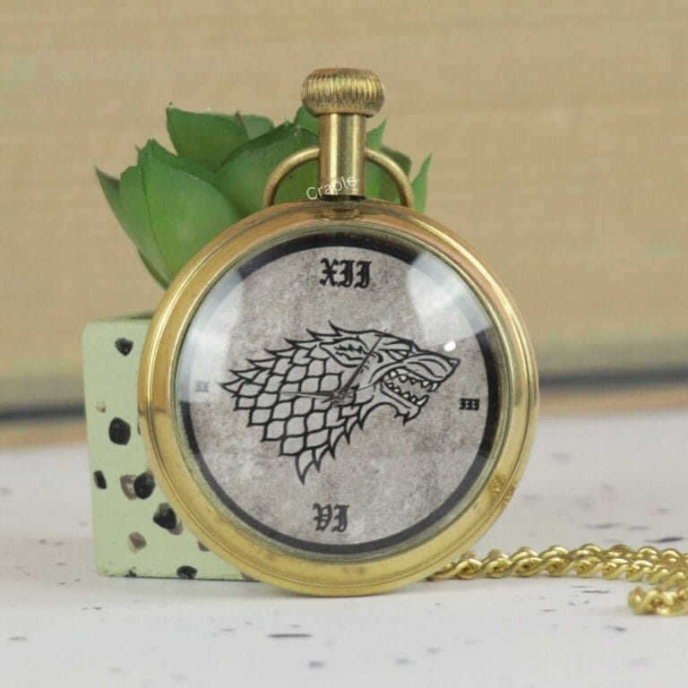 Vintage-style brass pocket watch featuring the Game of Thrones Direwolf sigil, resting against a decorative plant.