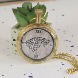 Angled side view of the brass Game of Thrones pocket watch, showing the crown and attached chain.