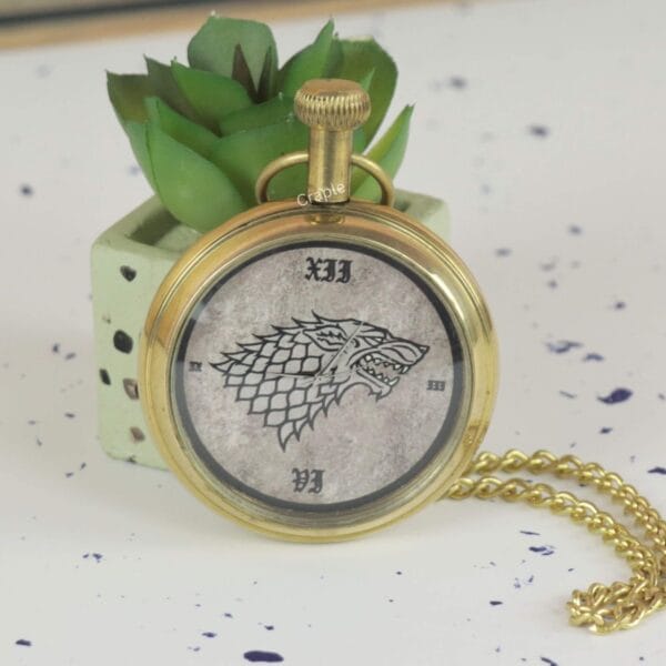 Angled side view of the brass Game of Thrones pocket watch, showing the crown and attached chain.