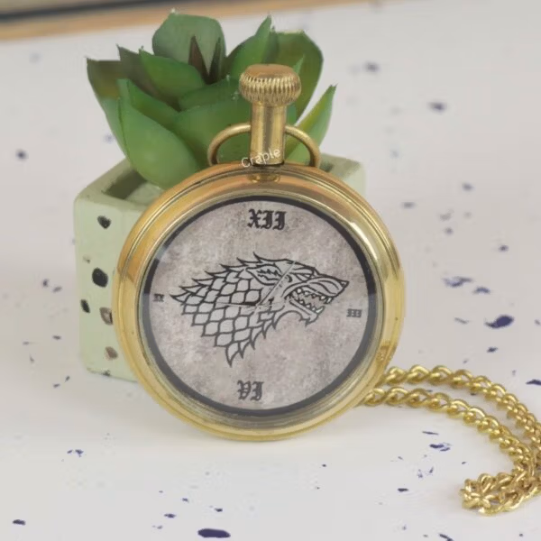 Angled side view of the brass Game of Thrones pocket watch, showing the crown and attached chain.