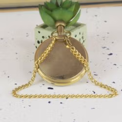 The back view of the shiny brass pocket watch with its chain elegantly draped over the top.