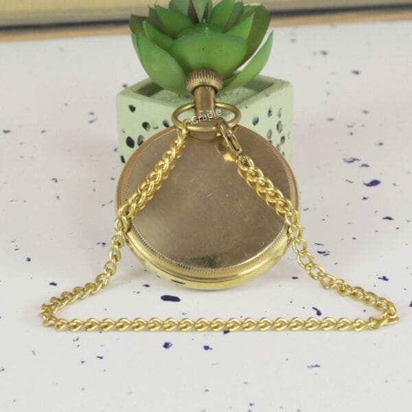 The back view of the shiny brass pocket watch with its chain elegantly draped over the top.