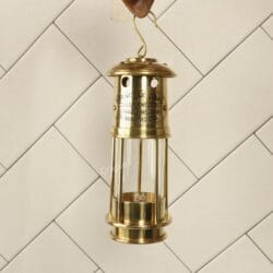 Handcrafted antique brass miner's lantern with a clear glass cylinder being held up by its top hanging hook.