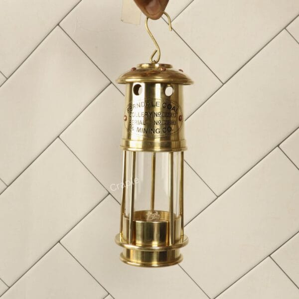 Handcrafted Antique Brass Miner’s Lantern-1 Handcrafted antique brass miner's lantern with a clear glass cylinder being held up by its top hanging hook.