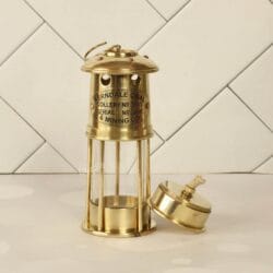 Angled view of the shiny brass miner's lamp with its oil burner base placed beside it at a tilt.