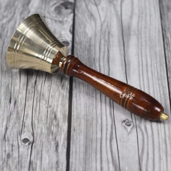 The brass and wood hand bell lying on its side, showcasing the smooth polished finish of the handle.
