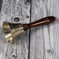 The golden brass school bell lying on a wooden table, with a focus on its traditional shape and finish.