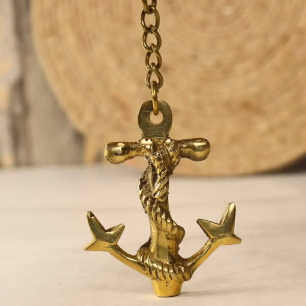 Front view of the nautical brass anchor keychain hanging from its chain against a rustic background.