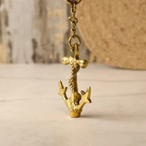 A low-angle view of the hanging brass anchor charm, emphasizing the shape of the flukes and the rope texture.