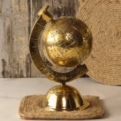The handmade brass world globe sitting on a rustic square jute coaster against a wooden background.