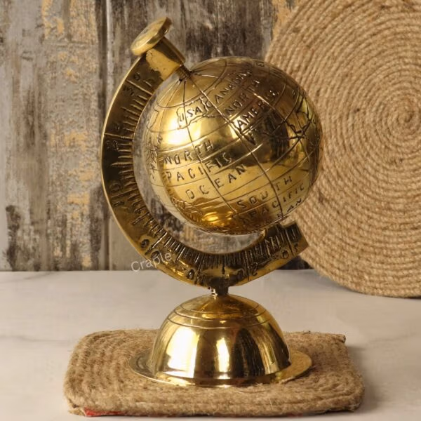 The handmade brass world globe sitting on a rustic square jute coaster against a wooden background.