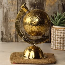 Angled side view of the shiny brass decorative globe, showing the numbered meridian arm next to a plant.