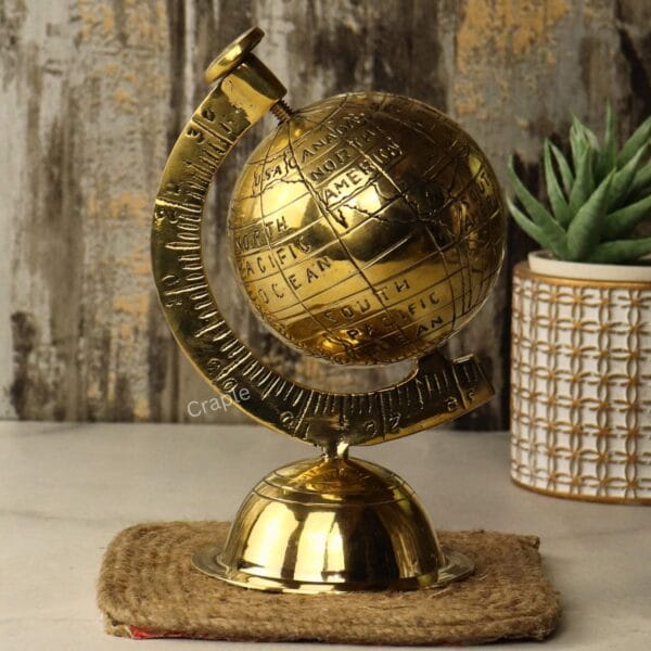Handmade Brass Decorative Globe-3 Angled side view of the shiny brass decorative globe, showing the numbered meridian arm next to a plant.