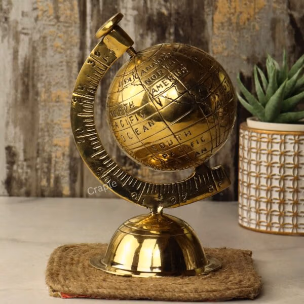Angled side view of the shiny brass decorative globe, showing the numbered meridian arm next to a plant.