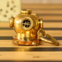 Handmade brass diver helmet keychain with a shiny finish and copper details, sitting on a wooden surface.
