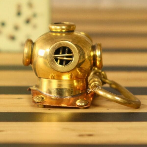 Handmade brass diver helmet keychain with a shiny finish and copper details, sitting on a wooden surface.