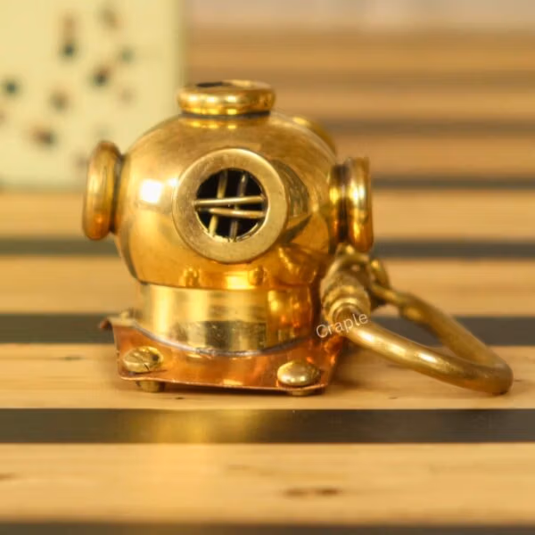 Handmade brass diver helmet keychain with a shiny finish and copper details, sitting on a wooden surface.