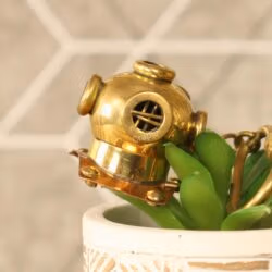 Vintage-style brass diver helmet keychain used as a charming decorative accessory on a small potted plant.