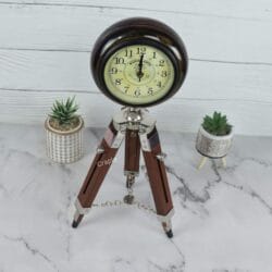 Angled perspective of the wooden tripod desk clock on a marble surface, shown with small decorative plants.