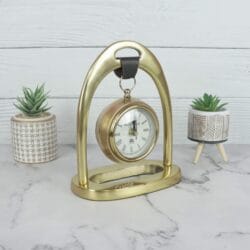 Front view of the golden tabletop clock with a hanging design, showing the elegant arch and stable base.