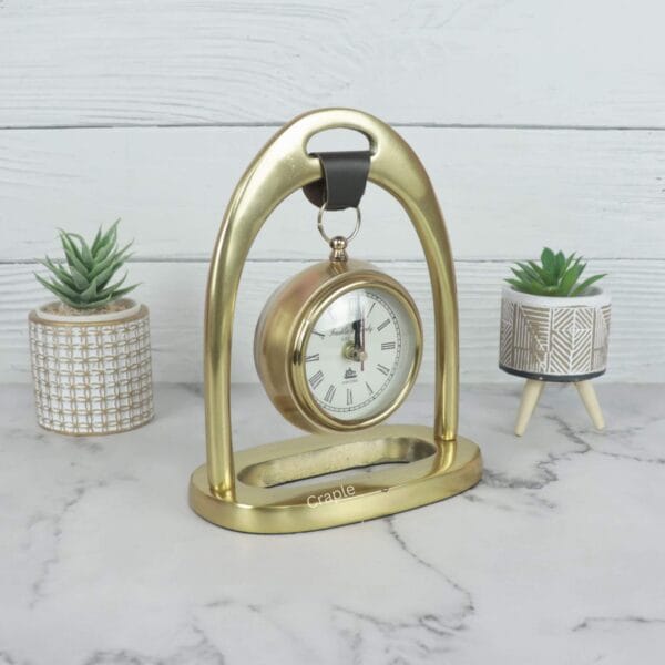 Front view of the golden tabletop clock with a hanging design, showing the elegant arch and stable base.