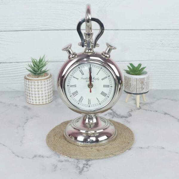 The nickel-plated aluminum stopwatch clock displayed as a decorative piece between two small potted succulents.