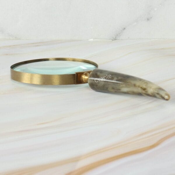 Vintage magnifying glass with a genuine curved horn handle and a shiny brass frame, resting on a marble surface.