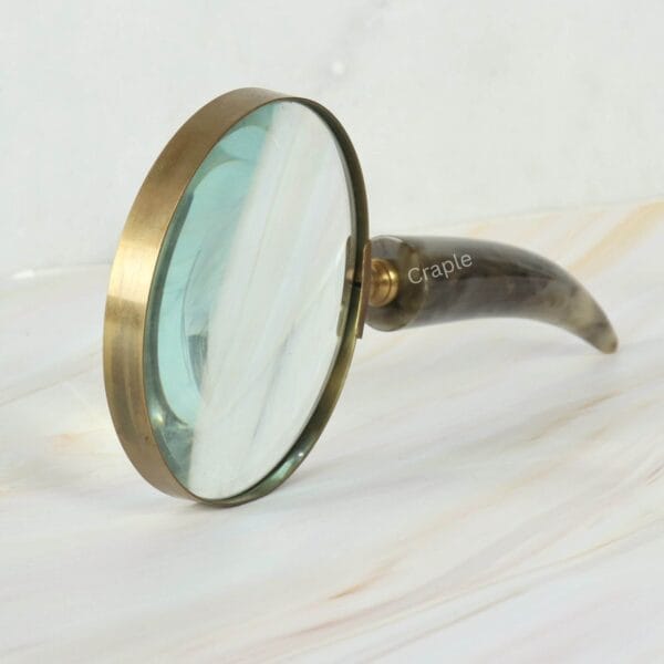 Handheld magnifier with a 5X lens and a polished horn handle, balanced upright on a tabletop.