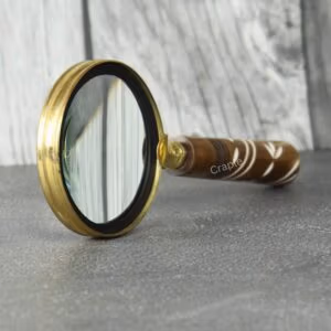 Vintage magnifying glass with a polished brass frame and an inlaid wood-style handle, standing upright on a slate surface.