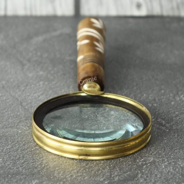 Handheld magnifier with a 5X lens and a polished wood handle featuring a white spiral inlay, lying flat.
