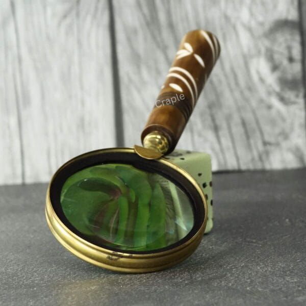 Angled view of the brass magnifying glass, showing the clarity of the 5X lens and the detailed craftsmanship of the handle.