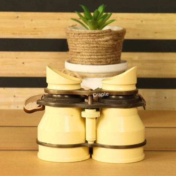 Side view of vintage light yellow aluminum binoculars with angled eyecups and brown leather strap – stylish retro decor accessory