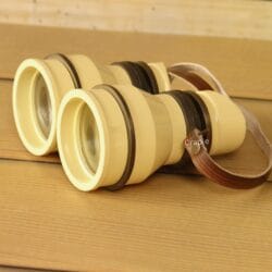 Retro light yellow aluminum binoculars with angled eyecups and leather strap on wooden table – vintage decorative binoculars for home decor or unique gift.