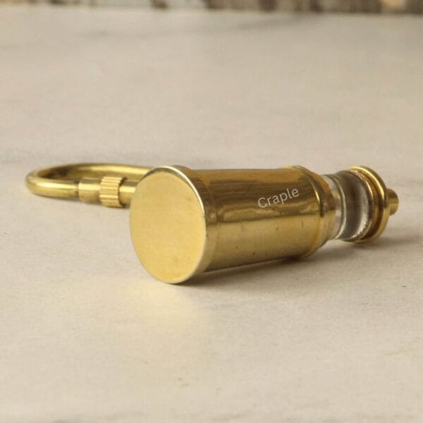 The brass lighthouse keychain lying on its side, showing the detail of its flat base and solid construction.