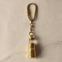 The miniature brass lighthouse keychain hanging from its secure carabiner clip against a neutral background.